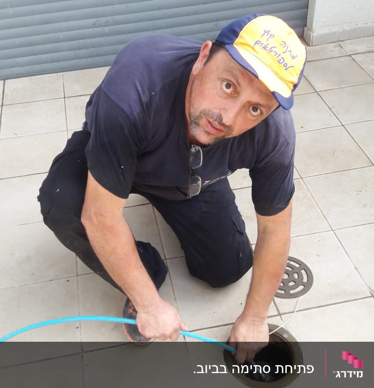 אדם עובד עם צינור ניקוז בפתח ביוב
